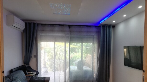 Una sala de estar moderna con un sofá, un televisor de pantalla plana y un ventanal corredero que da a un balcón.