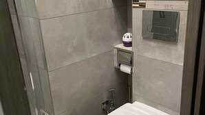 Un baño moderno con inodoro, secador de manos y un pequeño estante con artículos de tocador.