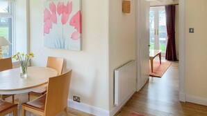 A dining area with a round table, chairs, a vase with yellow flowers, and a painting of pink flowers on the wall.