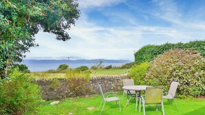 A patio with a table and chairs overlooking a grassy area with a stone wall and a view of the sea.