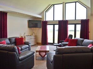 A living room with leather sofas, a coffee table, a TV, and large windows with curtains.