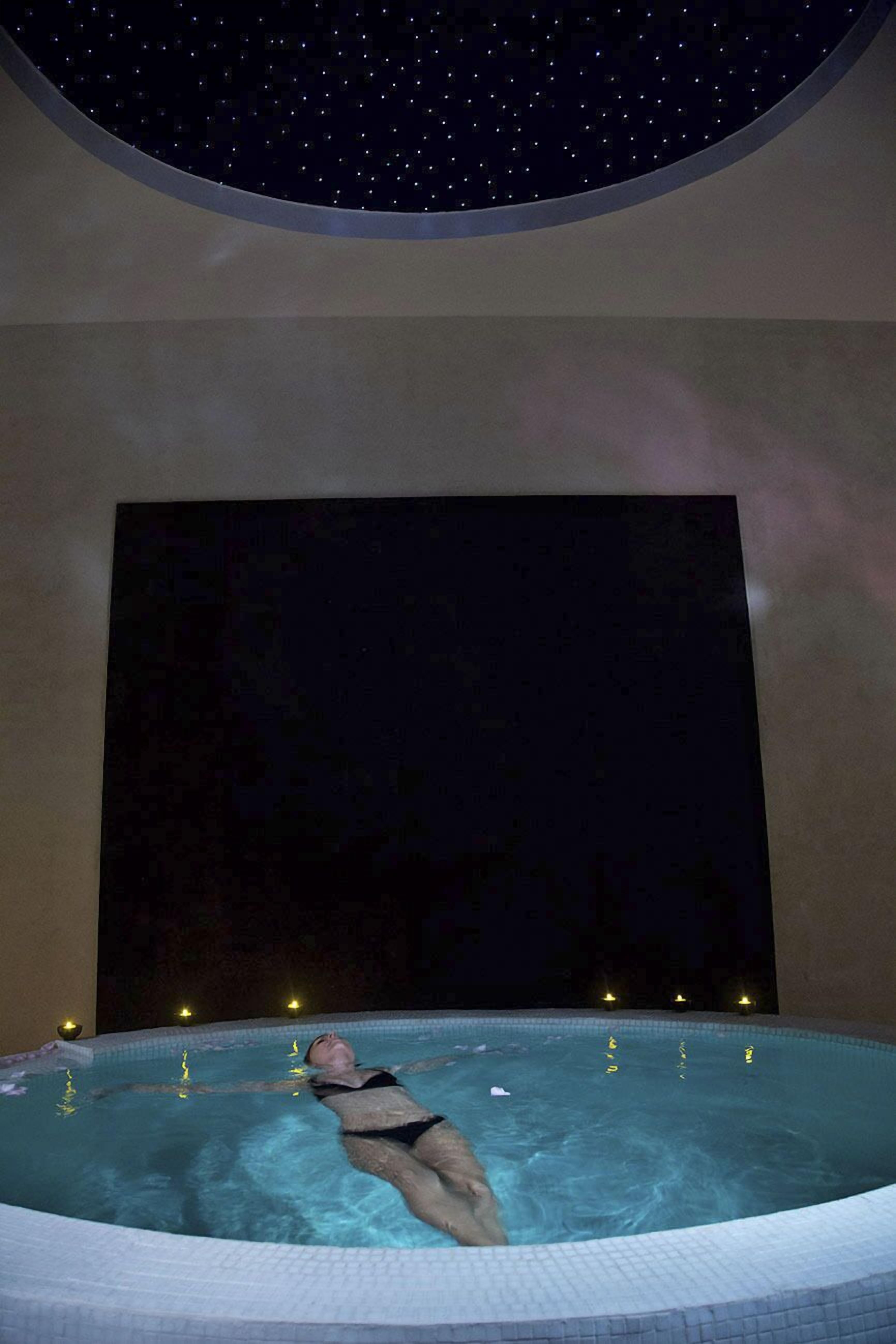 Iemand ontspant in een jacuzzi met een sterrenhemel en een donkere muur op de achtergrond.