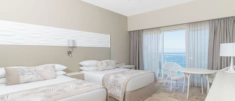 Ein Hotelzimmer mit zwei Betten, einem Schreibtisch, einem Stuhl, einem Deckenventilator und Blick auf den Ozean.
