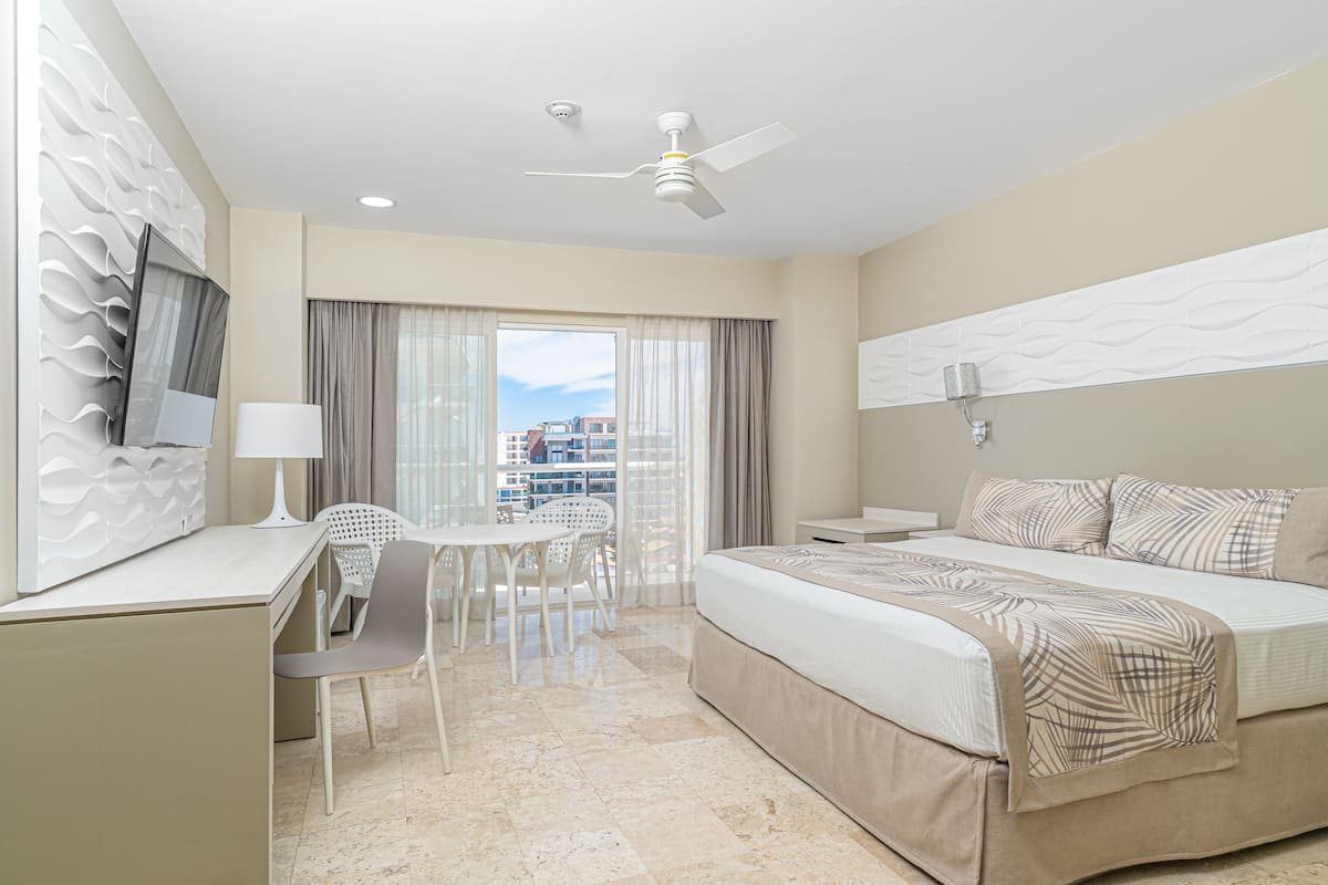 A hotel room with a bed, desk, chair, and a view of buildings through the window.