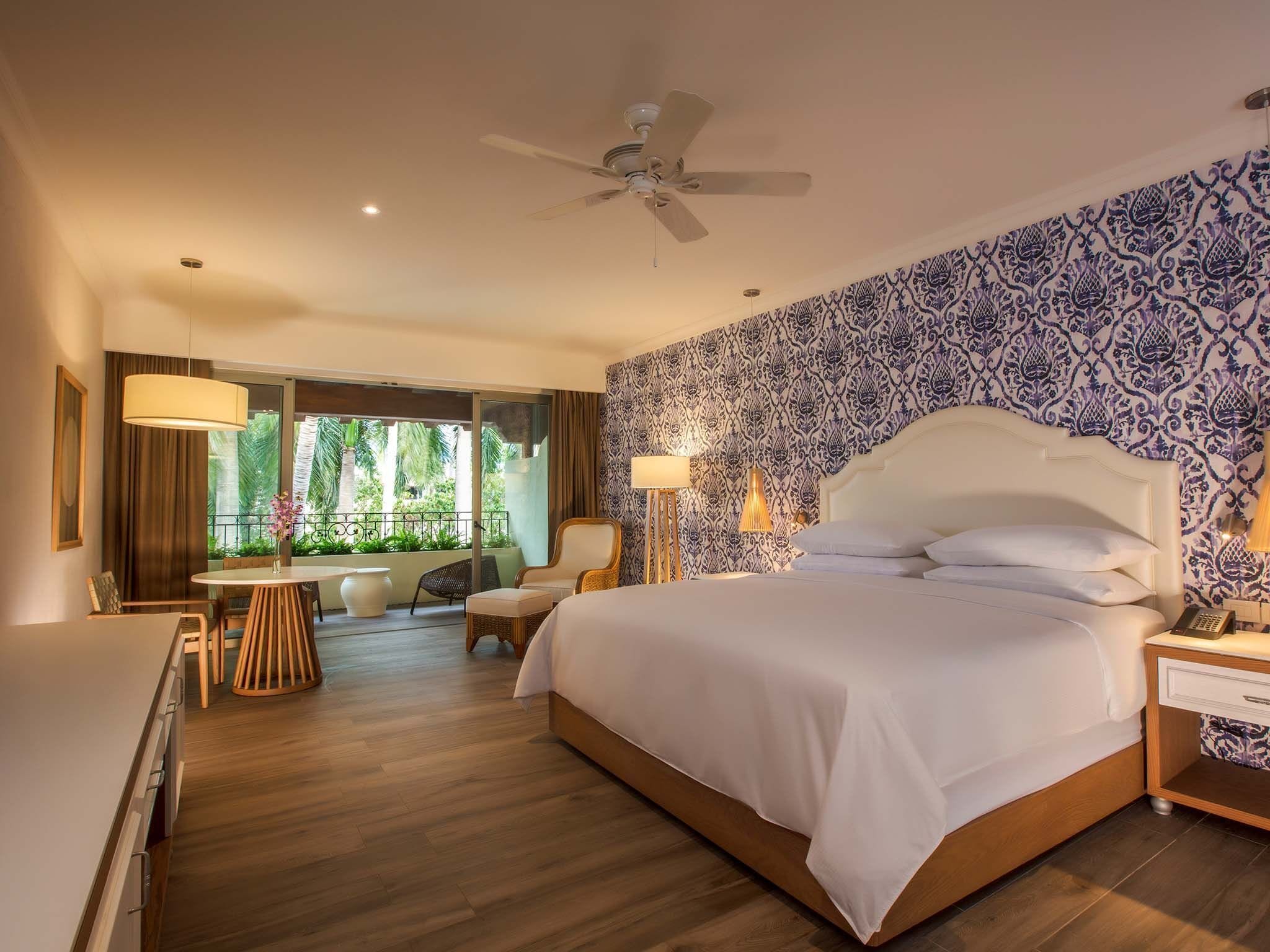 Una habitación de hotel con una cama grande, un balcón con mobiliario exterior y un papel tapiz estampado.