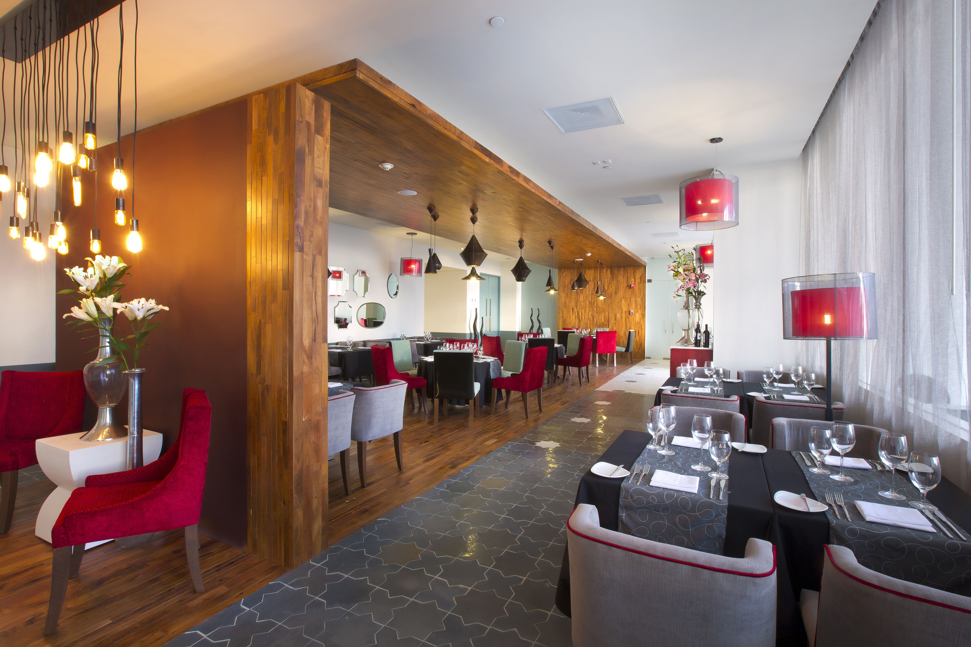 Un ristorante moderno con elementi in legno, sedie rosse e diversi tavoli apparecchiati per gli ospiti.