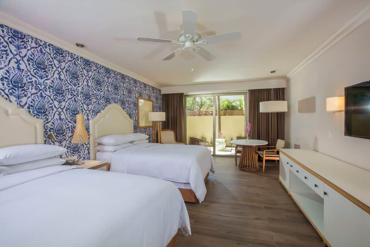 A hotel room with two beds, a ceiling fan, a TV, a dining area with a table and chairs, and a view of the outdoors.