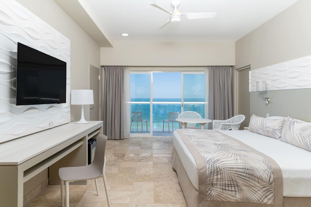 A hotel room with a bed, desk, chair, TV, and a balcony with a view.