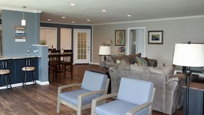 A living room with a blue sofa, two blue chairs, a coffee table, and a dining area with a table and chairs. - Discover Your Perfect Getaway! Beautiful Scenic Lakefront Condo (Montague)