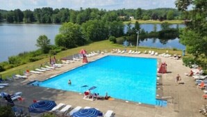 A swimming pool with lounge chairs and umbrellas, surrounded by greenery and a lake. - Discover Your Perfect Getaway! Beautiful Scenic Lakefront Condo (Montague)