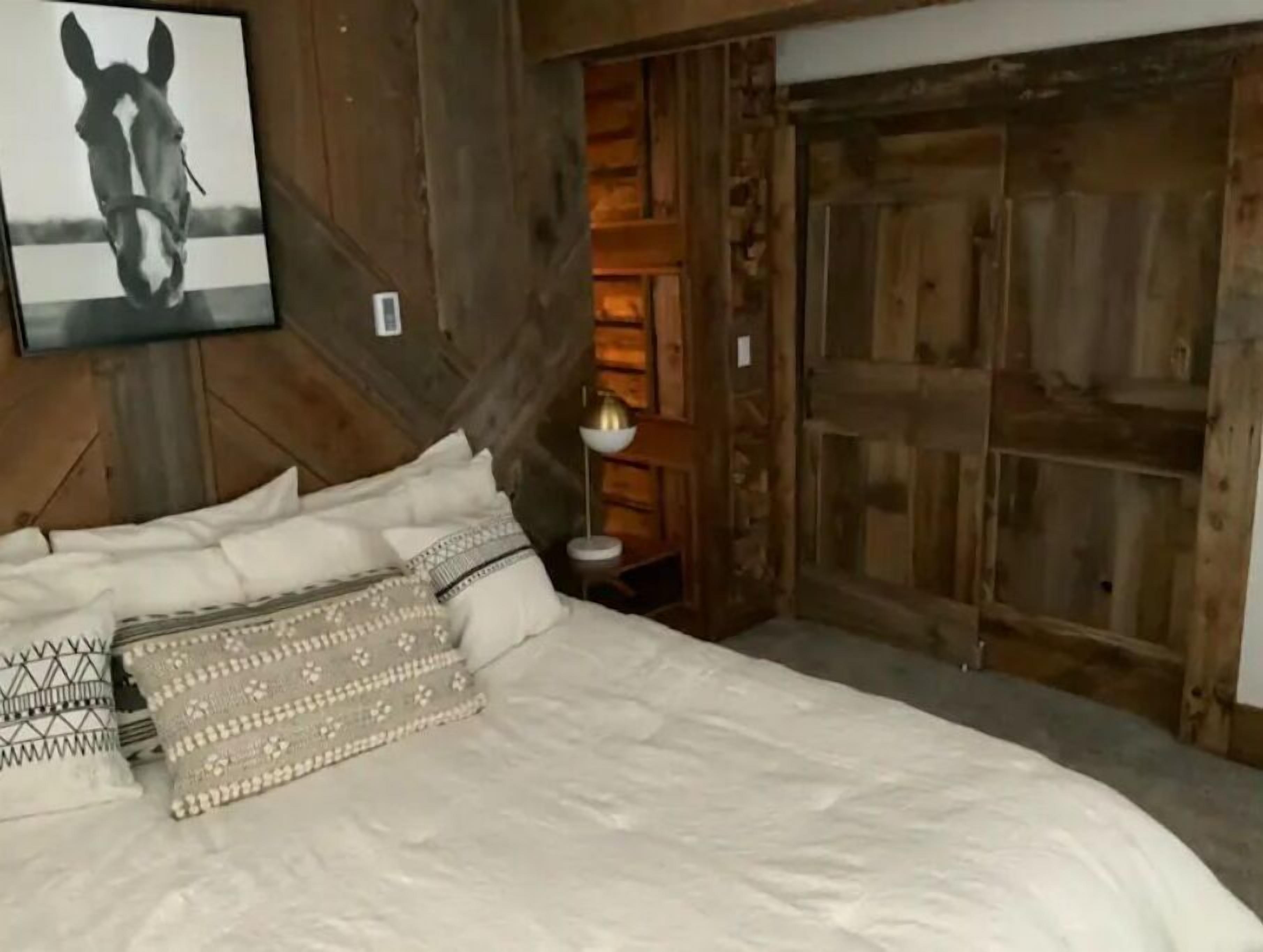 A bedroom with a large bed, wooden walls, and a horse-themed artwork.
