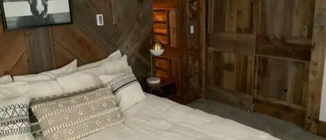 A bedroom with a large bed, wooden walls, and a horse-themed artwork.