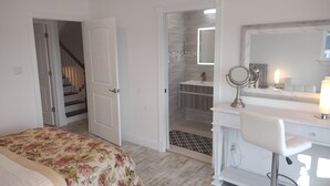 Un dormitorio con cama, un tocador blanco con espejo, y un baño con ducha e inodoro.