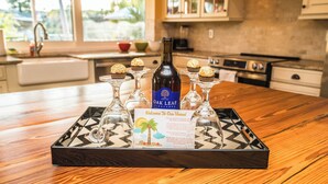 A tray with a bottle of Oak Leaf Vineyards wine, three glasses, and a welcome card on a wooden table in a kitchen.