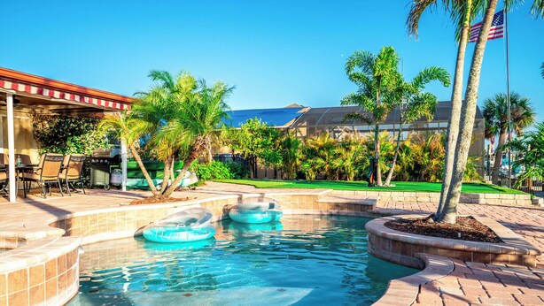 A swimming pool with inflatable rings, surrounded by palm trees and a patio area with outdoor furniture.