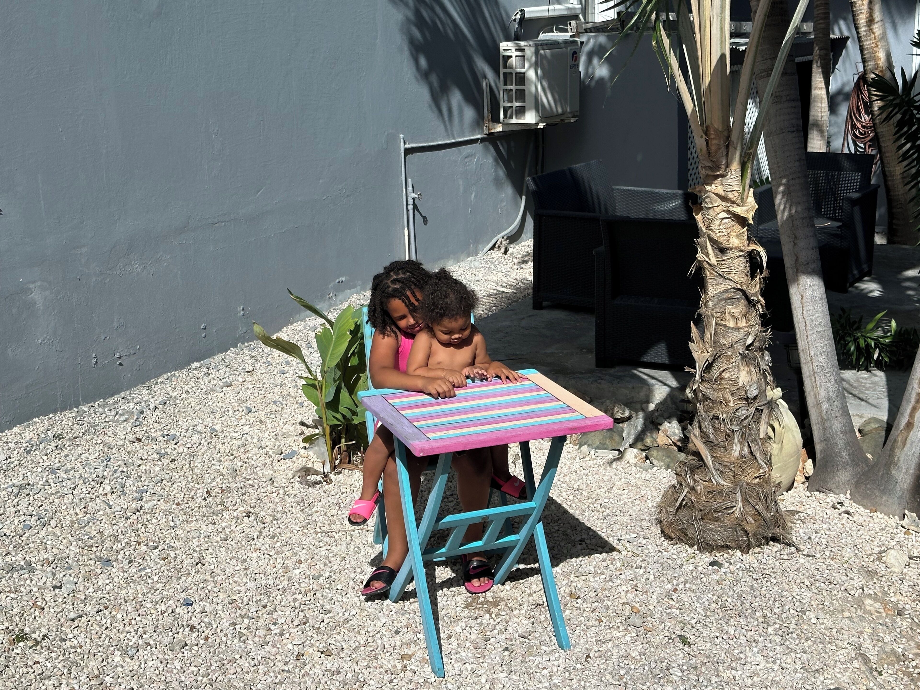 Two children sitting at a colorful striped table outdoors.