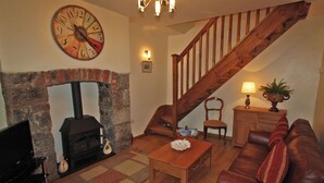 Ein Wohnzimmer mit Kamin, einer Holztreppe, einem Ledersofa und einer Wanduhr.