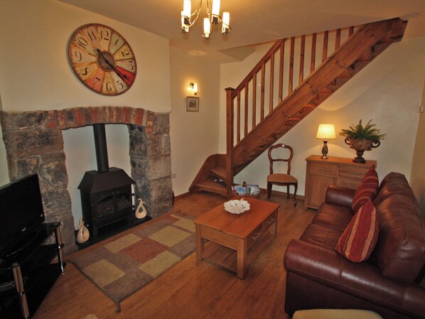 A living room with a fireplace, wooden staircase, leather sofa, and a clock on the wall.