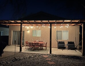 A covered patio with a wooden table and chairs, string lights, and a grill area. - Cheerful 3-bedroom vacation home (Tucson)