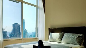 Een hotelkamer met een groot raam, een bed met kussens en een koffer op het bed.