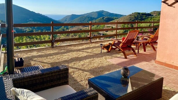 Un balcon agrémenté de meubles en osier, d’une table et offrant une vue sur des collines lointaines.