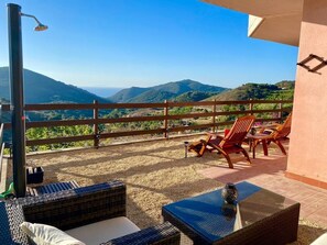 Ein Balkon mit Korbmöbeln, einem Tisch und Blick auf die fernen Hügel.