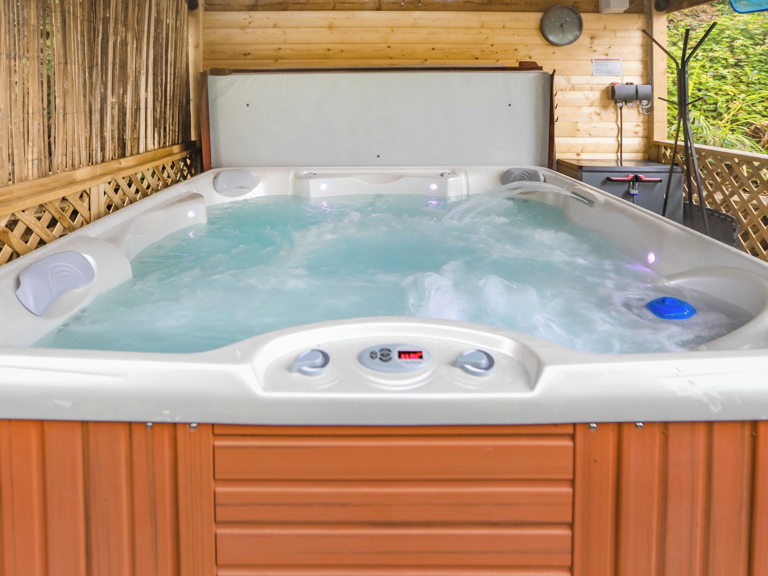A hot tub with a control panel, surrounded by wooden walls and a wooden deck.