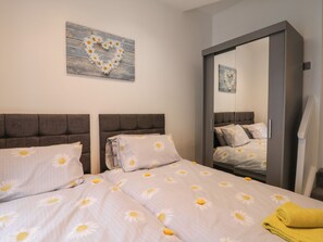 A bedroom with two beds, a heart-shaped wall decoration, and a mirror. - Daisy's Den (Whitby)