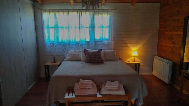 Ein Schlafzimmer mit einem großen Bett, Nachttischen, einem Heizkörper und einem Fenster mit Vorhängen.