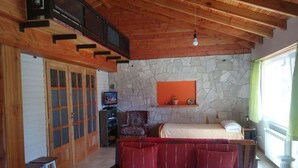Ein gemütliches Zimmer mit Steinwand, Holzboden, einer Couch, einem Bett und einem Fenster mit Vorhängen.