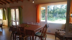 Ein Essbereich mit Holztisch und Stühlen, großen Fenstern mit Vorhängen und Blick ins Freie.