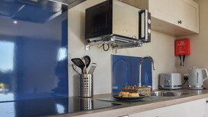 Eine moderne Küche mit einem Edelstahlherd, einer Mikrowelle, einem Wasserkocher und einem Toaster. An der Wand hängt eine Branddecke und auf der Arbeitsfläche steht ein Küchenhelferhalter.