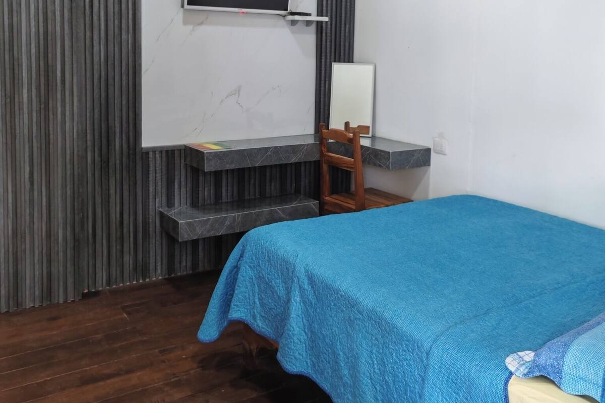 Un dormitorio con cama, escritorio, silla, televisor y aire acondicionado.