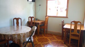 Un comedor con una mesa redonda, cuatro sillas de madera, un televisor montado en la pared y un ventanal que deja entrar luz natural.