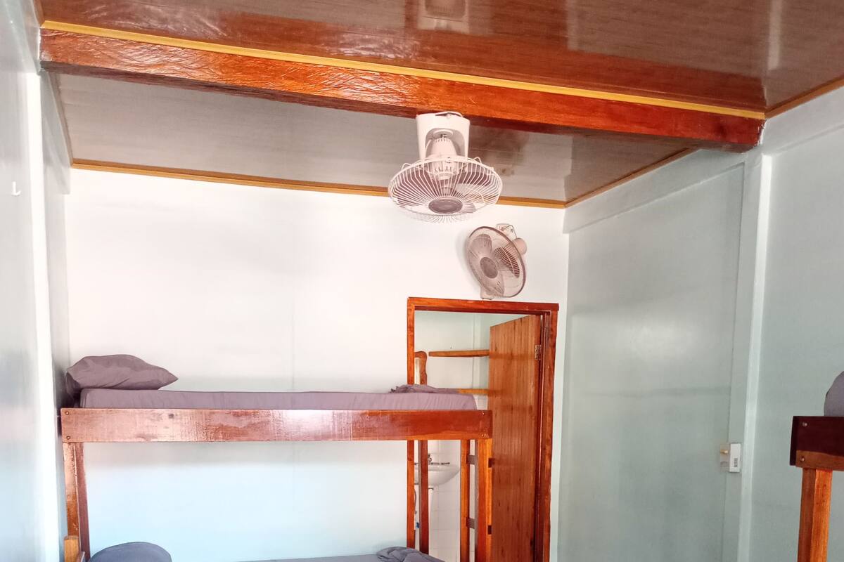 Una habitación con dos literas, una mesa de madera y un ventilador de techo.