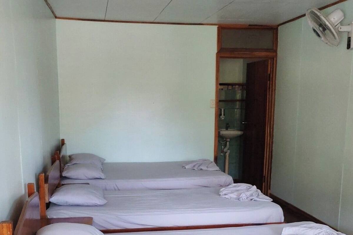 Una habitación con cuatro camas literas de madera, cada una con colchón y almohada blancos. Hay un ventilador de techo y un aire acondicionado de pared.