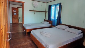 Una habitación con dos camas de madera, un ventilador de techo y una puerta que da a un baño.