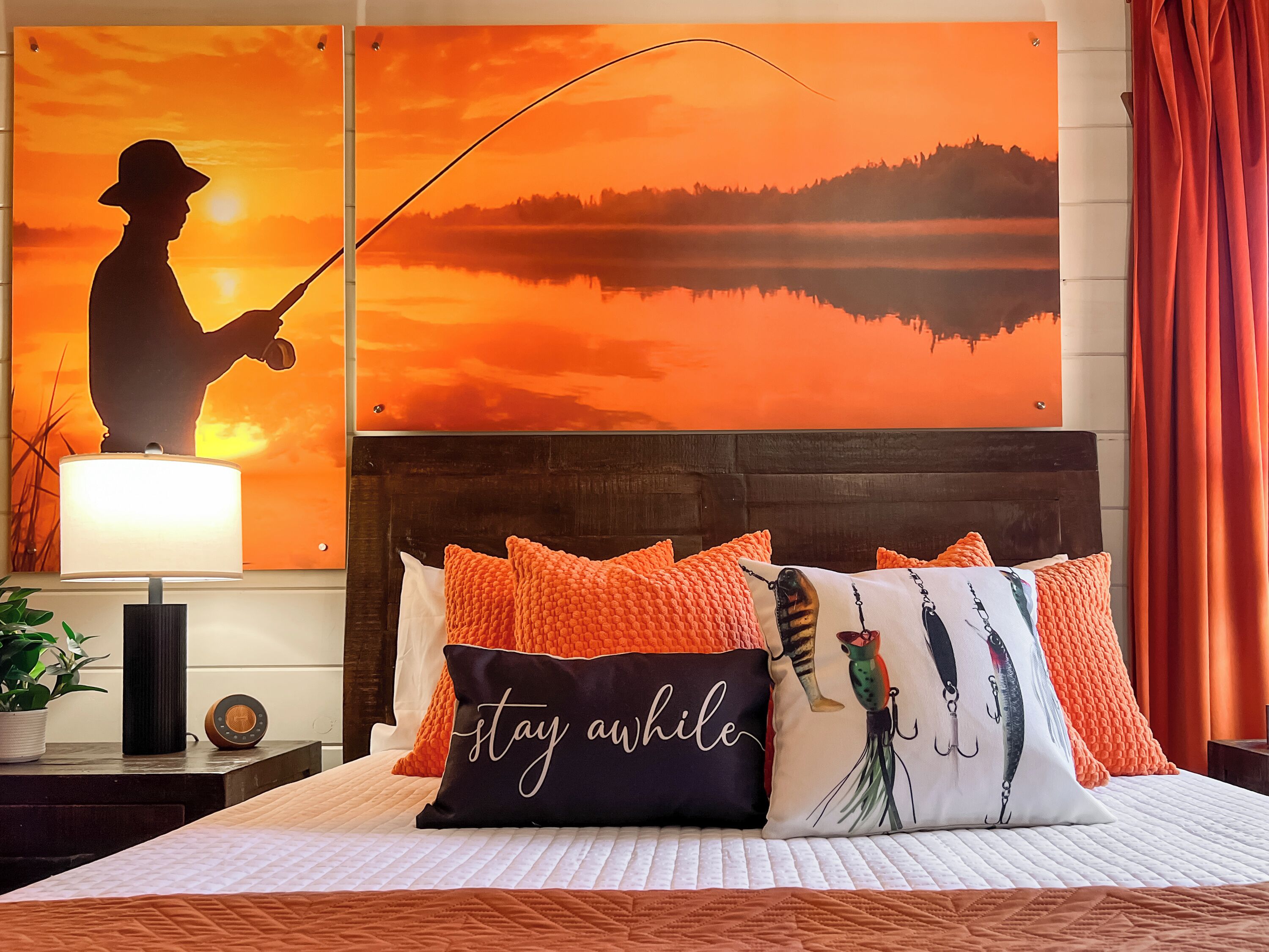 A bedroom with a bed, pillows, a nightstand, a lamp, and a painting of a fishing scene.