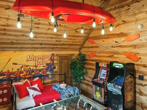 A cozy room with a bed, a foosball table, a game console, and a poster of 'Adventure Hollow'.