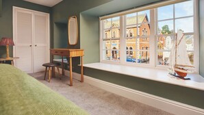A bedroom with a large window, a desk, a chair, a bed, and a small table with a lamp. - Waterfront Apartment (Fowey)