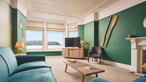 A living room with a green wall, a television, a wooden coffee table, and a blue sofa. - Waterfront Apartment (Fowey)