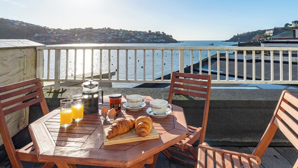 A wooden table with breakfast items and a view of the sea. - Waterfront Apartment (Fowey)