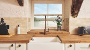 A kitchen with a view of a lake, a sink, a toaster, and a vase with flowers. - Waterfront Apartment (Fowey)