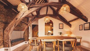 A rustic dining room with a wooden table and chairs, a patterned rug, and exposed wooden beams. - Waterfront Apartment (Fowey)