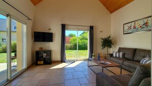 Ein geräumiges Wohnzimmer mit großen Schiebegläsern zum Garten, einem an der Wand montierten Flachbildfernseher, einem braunen Sofa und einem Couchtisch.