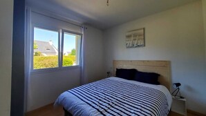Ein Schlafzimmer mit großem Fenster, einem Bett mit gestreifter Bettdecke, einem hölzernen Kopfteil, einem Nachttisch mit Lampe und einem Gemälde an der Wand.