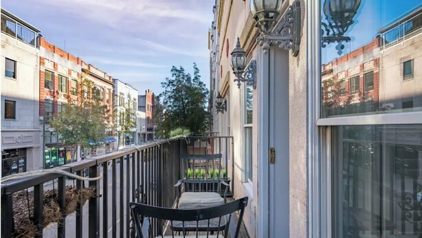 Een balkon met een stoel en een kleine tafel, met uitzicht op een straat met gebouwen.