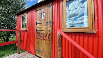 A red metal building with a wooden door, a window, and a small window above the door.