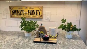 Eine Küche mit weißen Schränken, einer Arbeitsplatte aus Granit, einem Schild mit der Aufschrift 'Honey' und zwei Blumentöpfen.