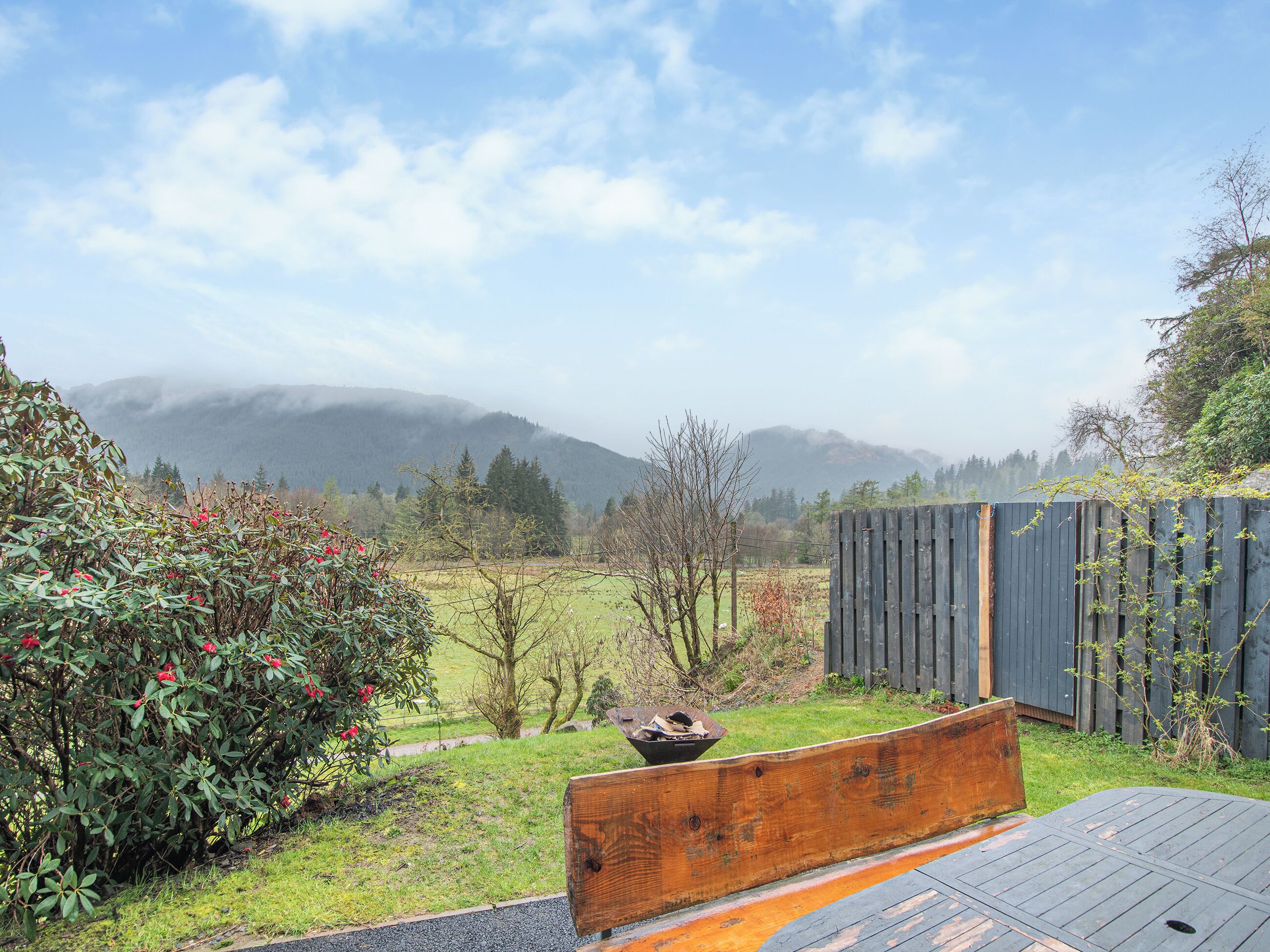 A wooden bench in a garden with a view of mountains and a wooden fence.